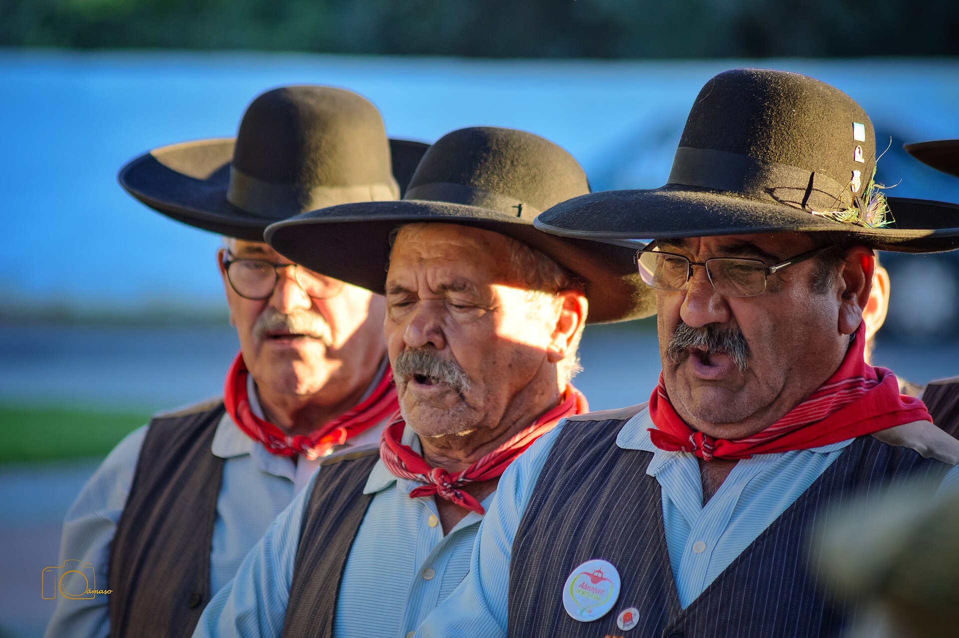 Cantadores alentejanos de chapéu e lenço vermelho a cantar em grupo